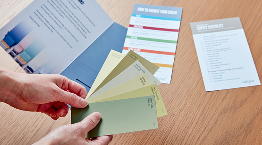 Hand holding color chips next an open color brochure.