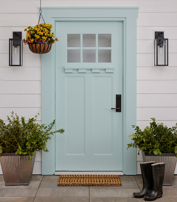 White siding home with exterior door in spring color, Aquatic Edge, spring flowers in hanging basket and potted greenery.